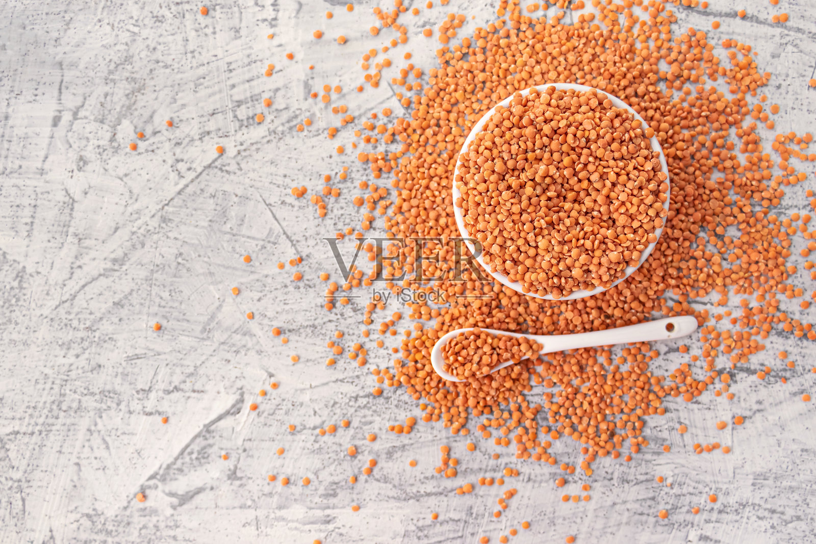 白色的石头背景上的白色盘子和勺子上的红色小扁豆。素食超级食物。照片摄影图片