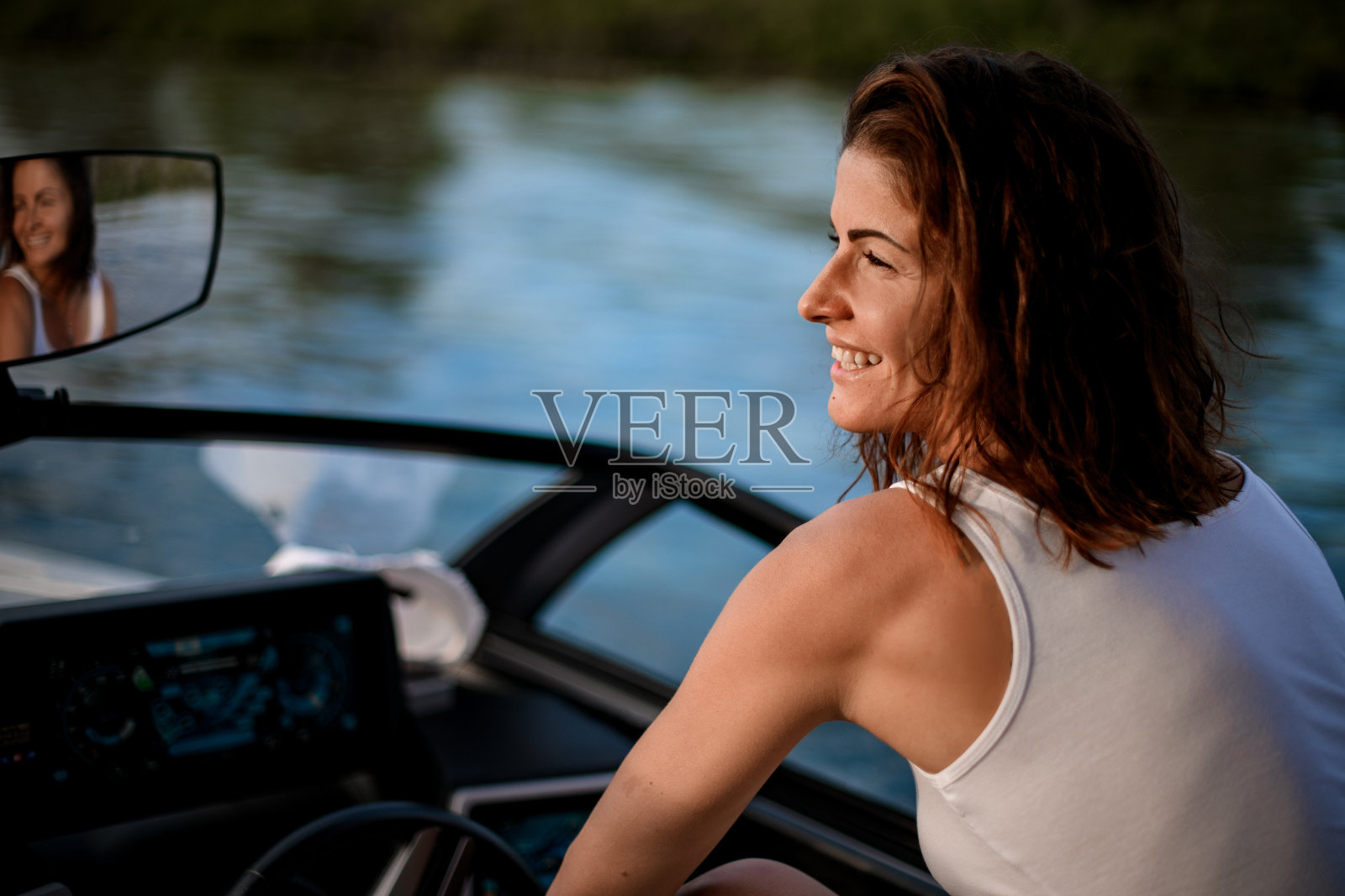 年轻微笑的女人坐在摩托艇的方向盘的特写。照片摄影图片