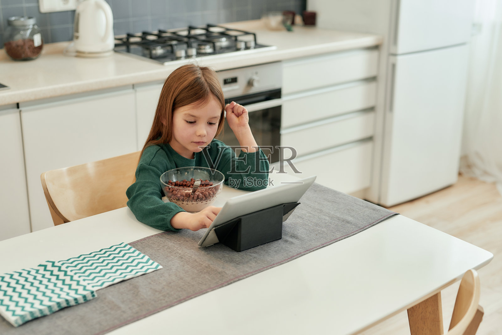 一个可爱的小女孩选择看什么在她的平板电脑早餐坐在厨房在远程教育独自照片摄影图片