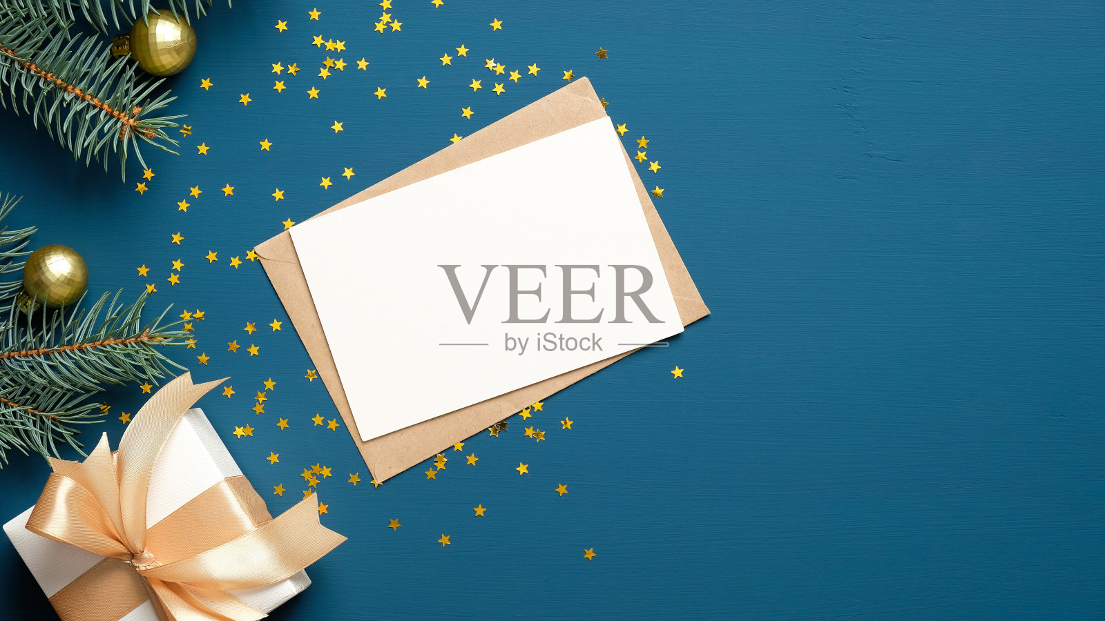 圣诞信信封用空白纸卡，白色礼盒用金色丝带蝴蝶结，冷杉树枝上装饰的球在深蓝色的背景。平躺，俯视图。给圣诞老人写信的概念。照片摄影图片