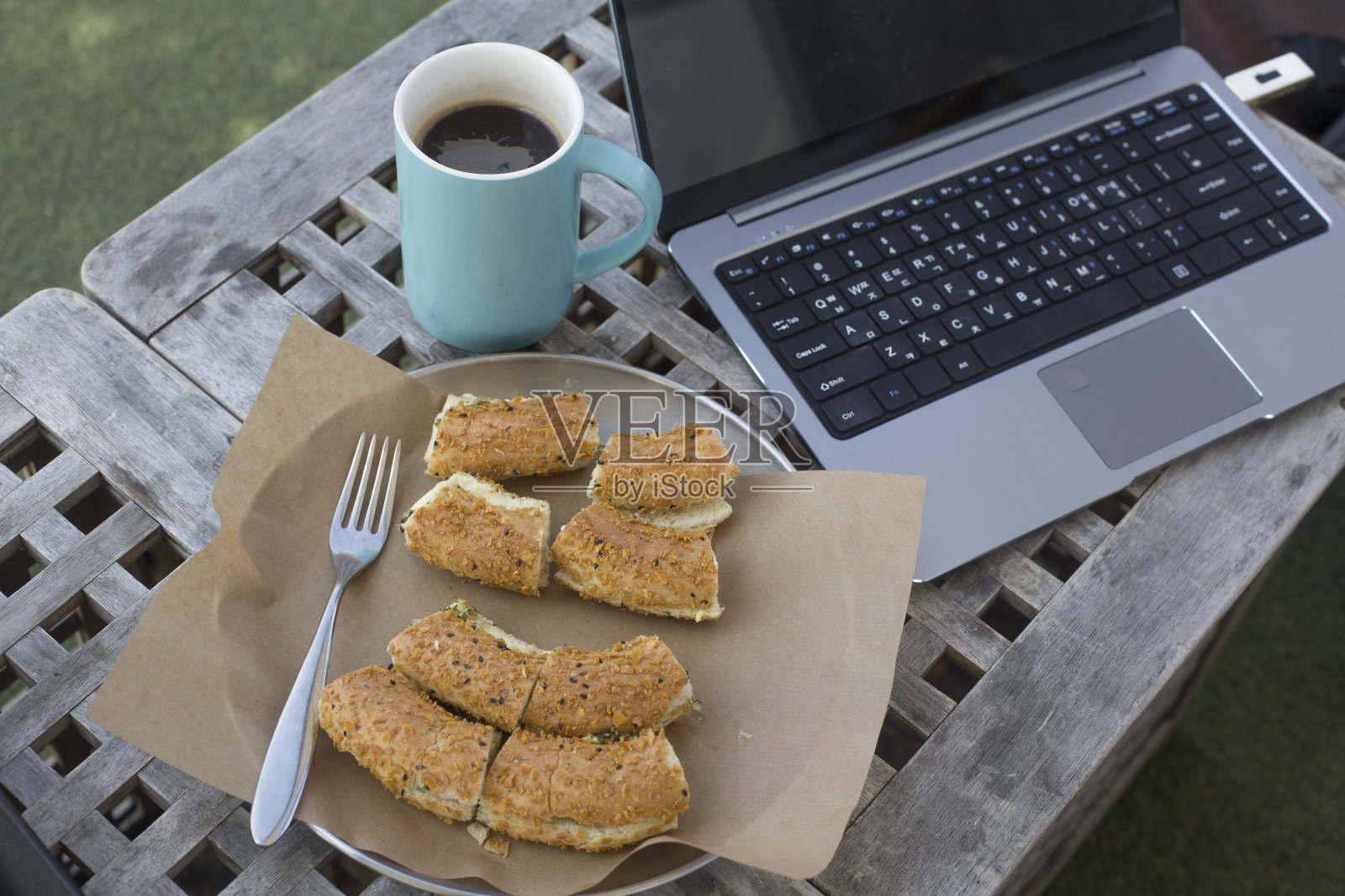打开笔记本电脑，面包和咖啡，户外背景。照片摄影图片