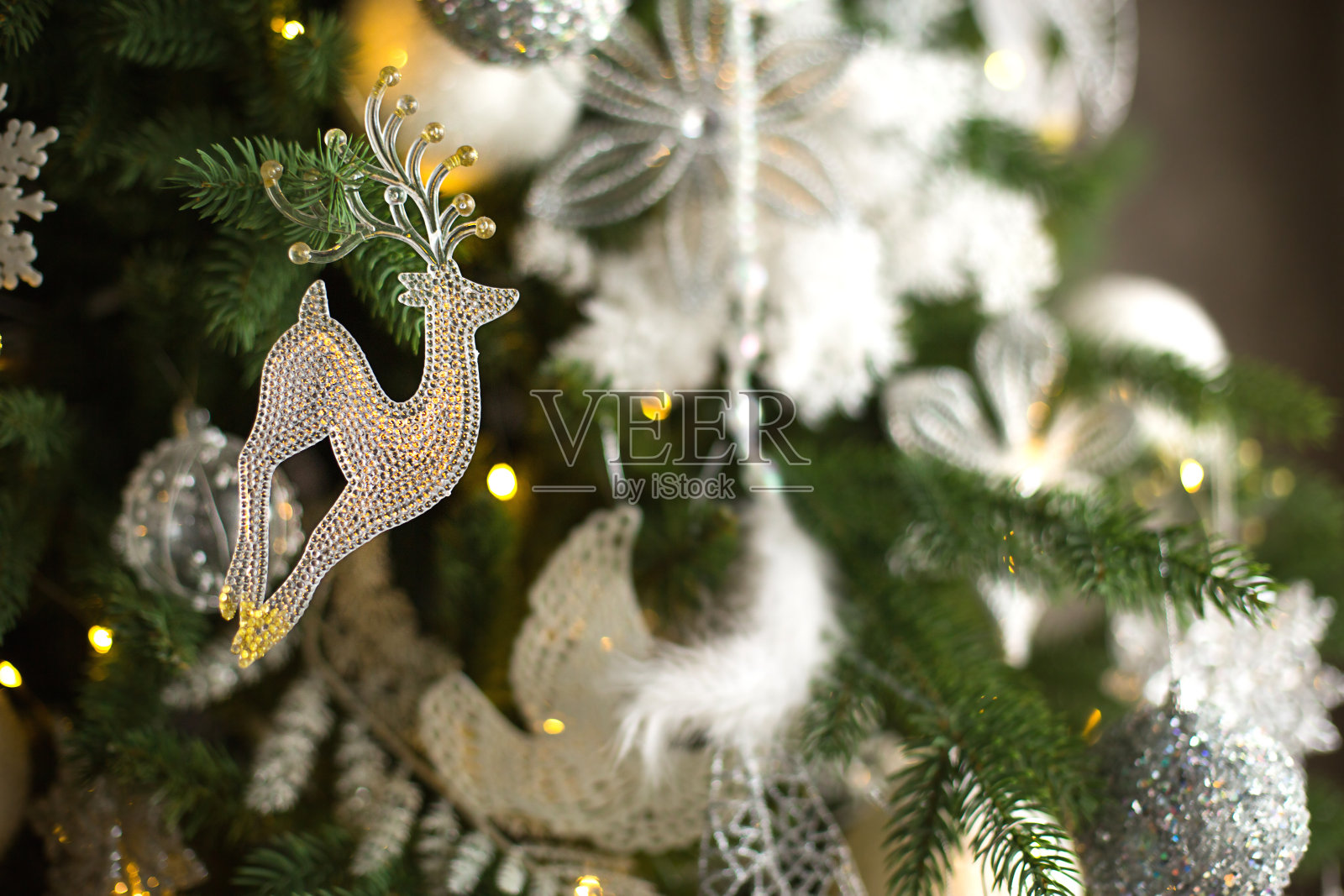 透明玻璃鹿吊坠在圣诞树上与灯花环。照片摄影图片