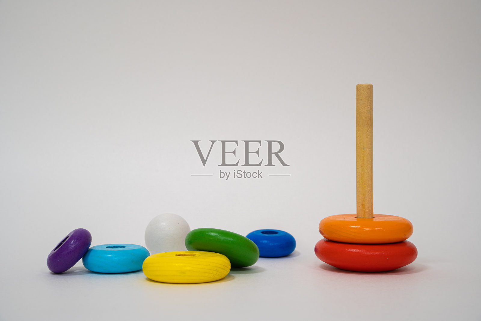 儿童木制玩具。彩色的环孤立在白色的背景。金字塔由彩色的木环建造，顶部有一个小丑的头。玩具婴儿和学步儿童愉快地学习机械技能照片摄影图片