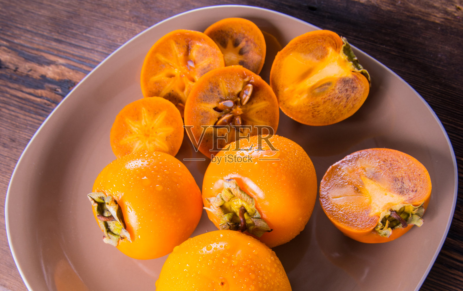 柿子用水珠切成两半放在盘子上的木桌上俯视特写，复制空间照片摄影图片