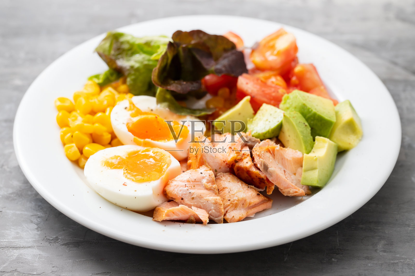 沙拉三文鱼配蔬菜和煮鸡蛋放在陶瓷背景的白色盘子上照片摄影图片