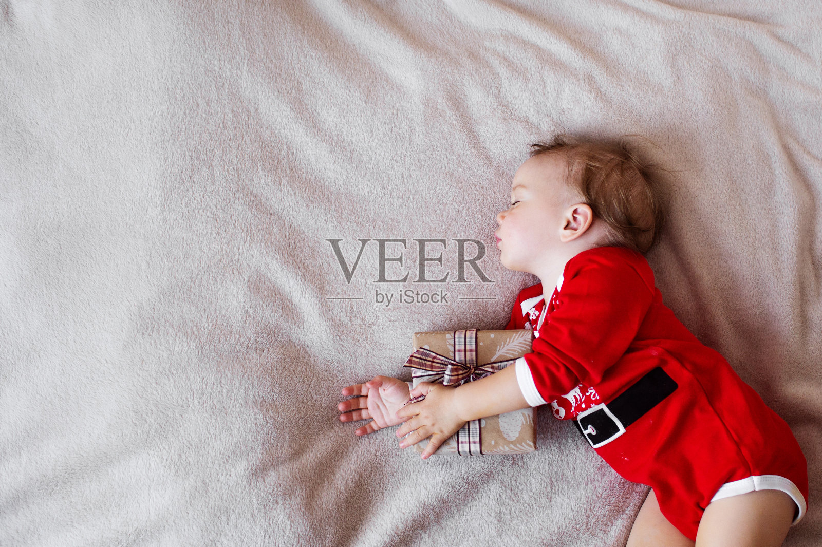 一个小女孩穿着圣诞老人的衣服睡在床上，抱着一份圣诞礼物照片摄影图片