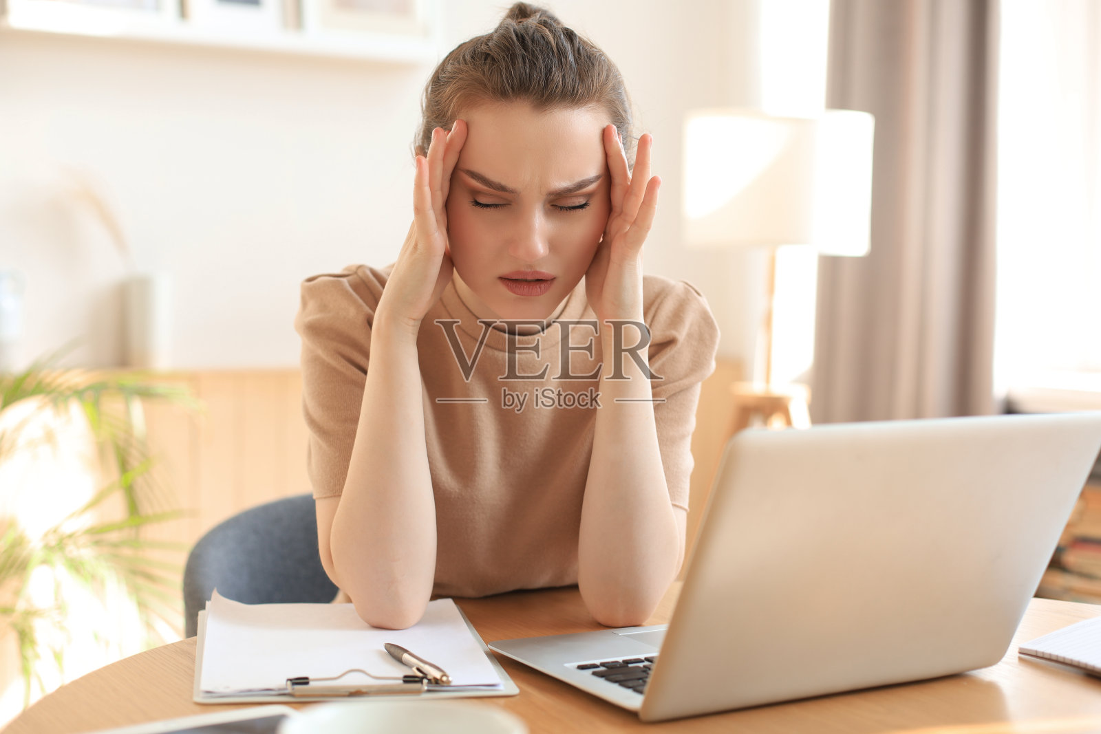 疲惫的年轻女学生坐在桌子上，倚靠着头的手，在休息时间休息在家里。照片摄影图片