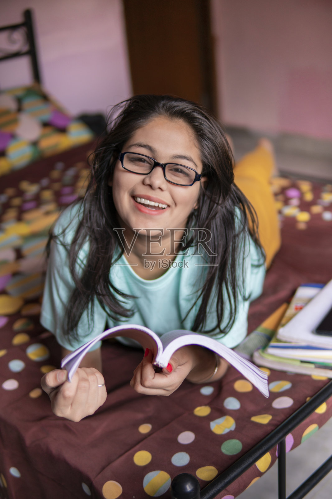 快乐的小女孩看书，躺在床上看着照相机。照片摄影图片