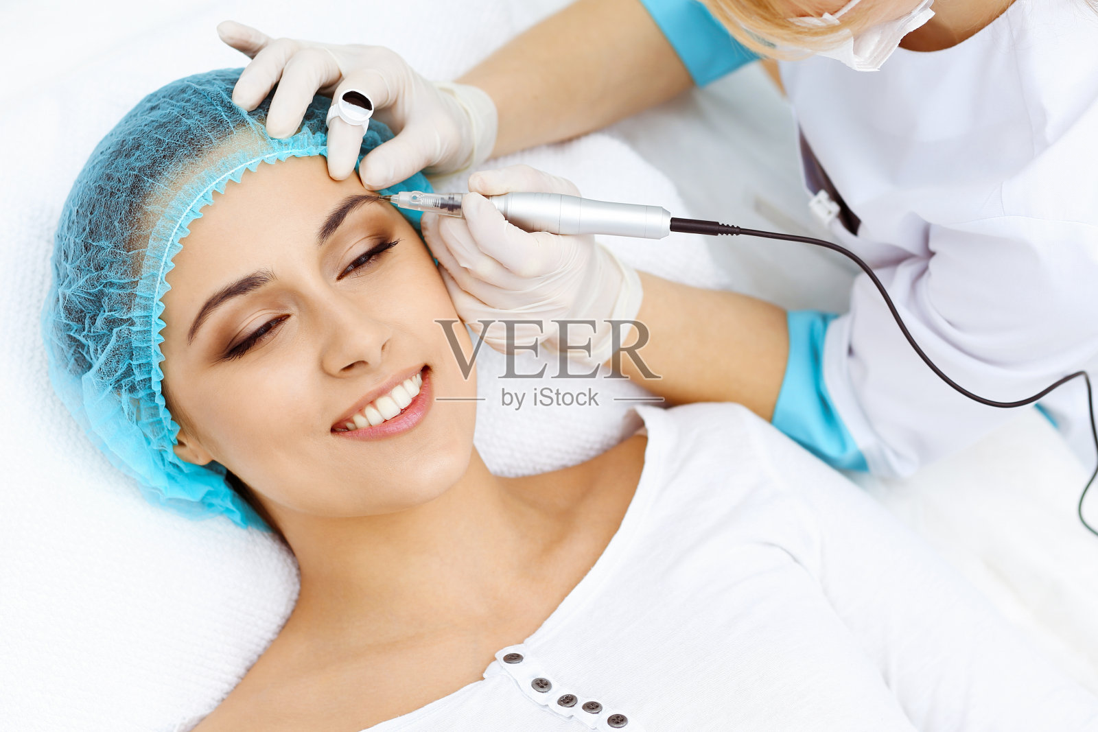 专业美容师在女人脸上纹眉。美容院永久眉妆，特写。美容治疗照片摄影图片