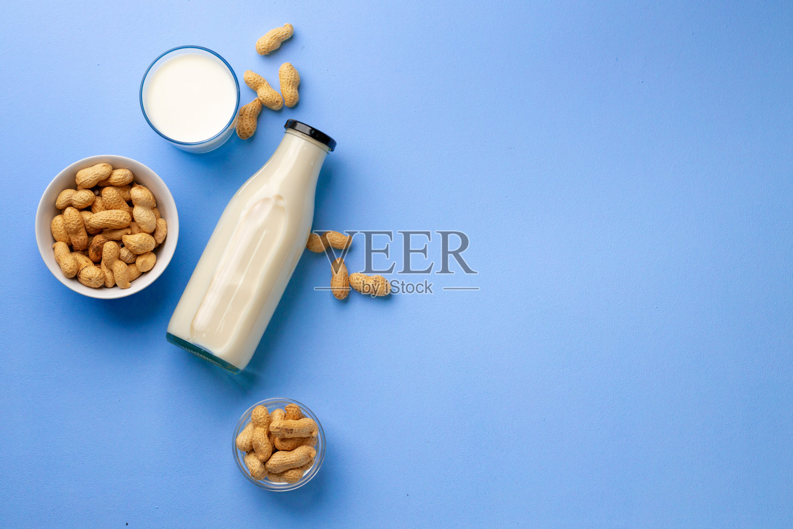 非乳脂牛奶，玻璃瓶，碗花生在蓝色的背景照片摄影图片