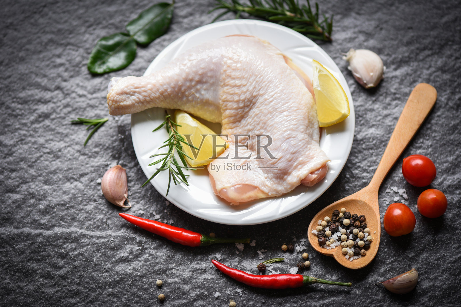 生鸡腿放在白色盘子里，用于烹饪泰国亚洲食物，迷迭香鸡，柠檬木餐桌上的食物照片摄影图片