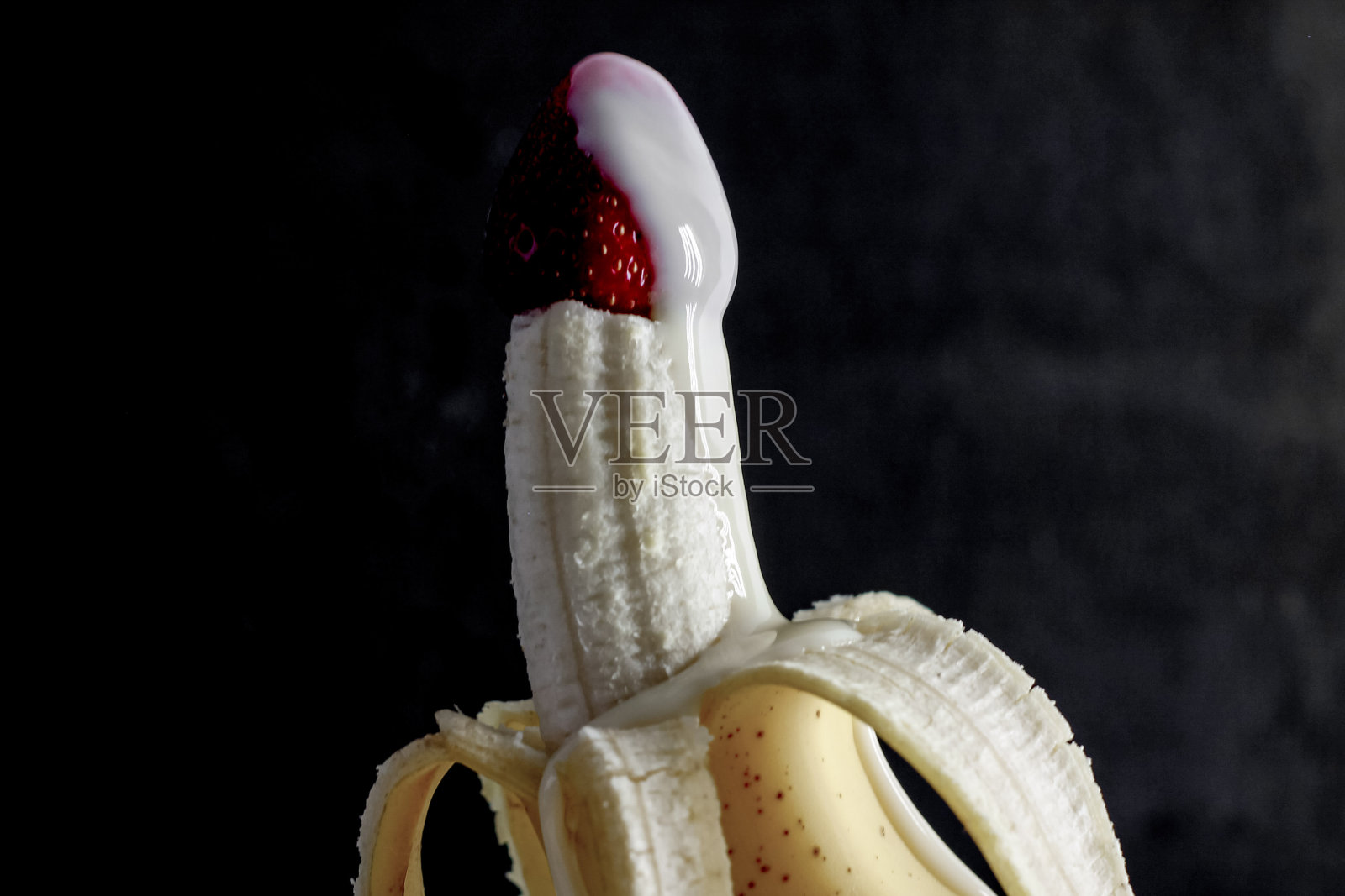 熟透的香蕉和红草莓撒上奶油，点缀在黑色的背景上照片摄影图片