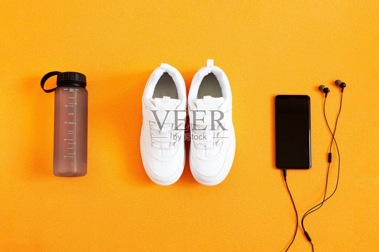 运动鞋，水瓶，带耳机的智能手机背景是橙色的健身垫。平铺构图。运动理念、健身理念、健康生活方式。前视图。照片摄影图片