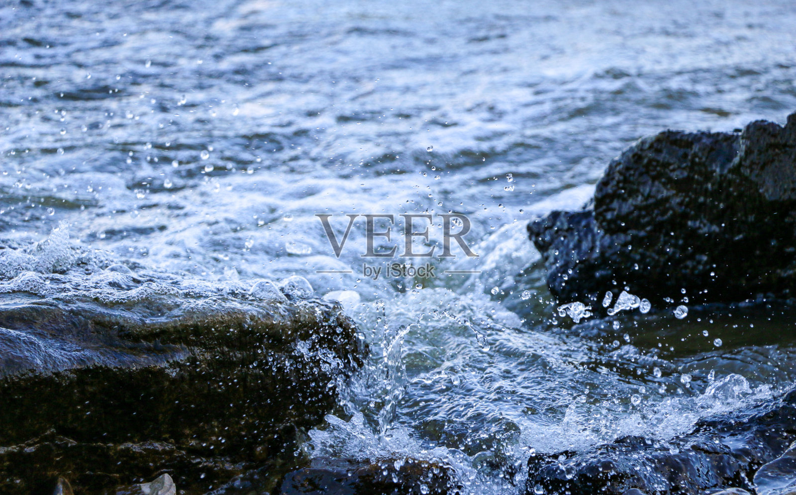 海浪冲上海岸，撞击岩石，在海岸附近产生许多水花和水花。在暴风雨的天气里，在带有泡沫和溅起水花的石头海岸附近的河上冲浪。照片摄影图片