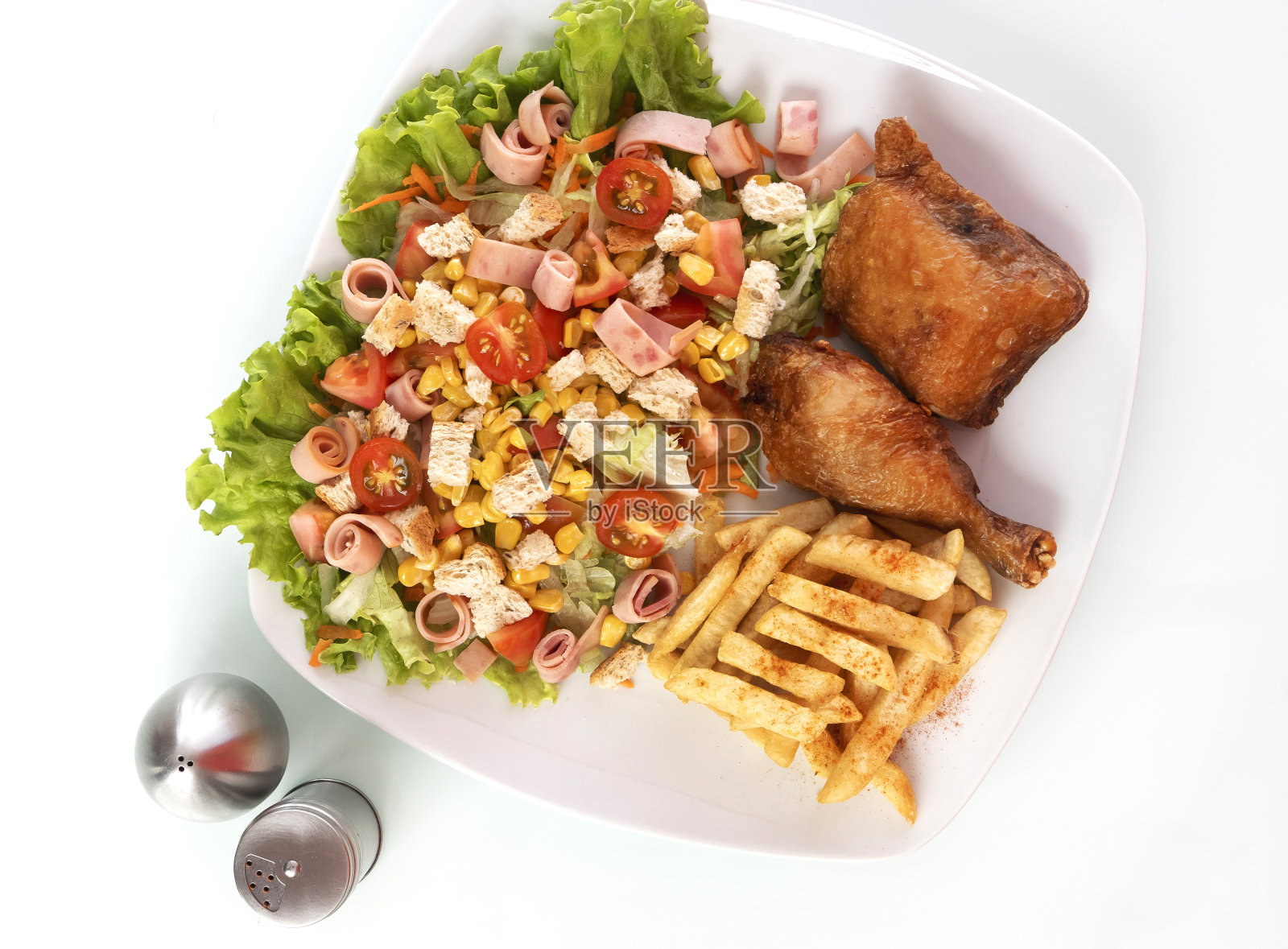 白桌子上的白盘子里装着鸡肉、米饭、沙拉和炸薯条，配上盐和胡椒照片摄影图片