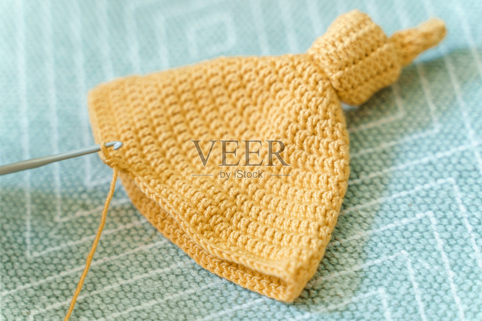 在薄荷背景上为婴儿钩针黄色帽子。照片摄影图片