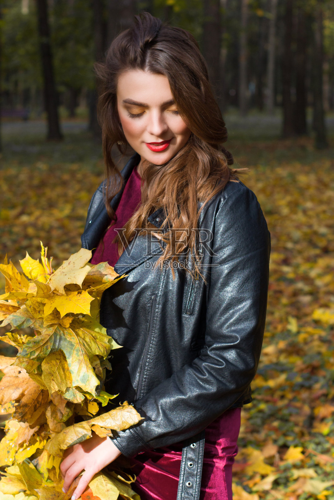 年轻的褐发女人肖像在秋天的颜色。手里拿着黄叶。照片摄影图片