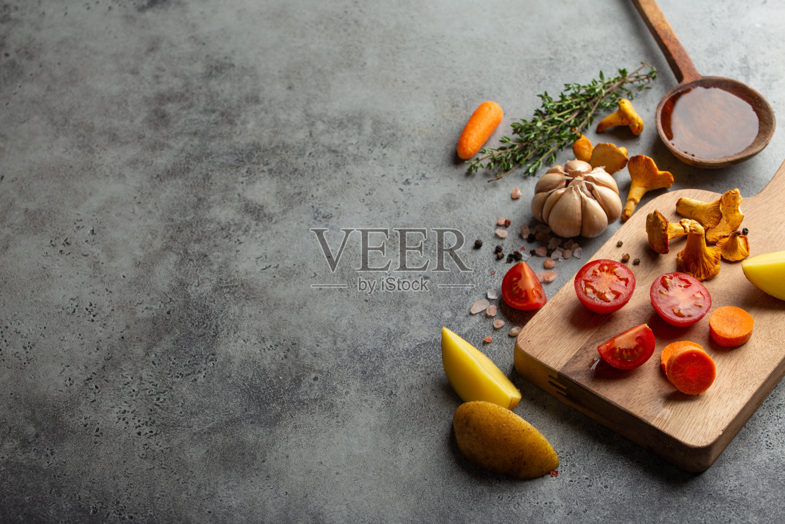 新鲜的圣女果、土豆、蘑菇、鸡油菌、胡萝卜、香草放在切菜板上，用木勺蘸橄榄油。食材烹饪背景，俯视图，文字空间照片摄影图片