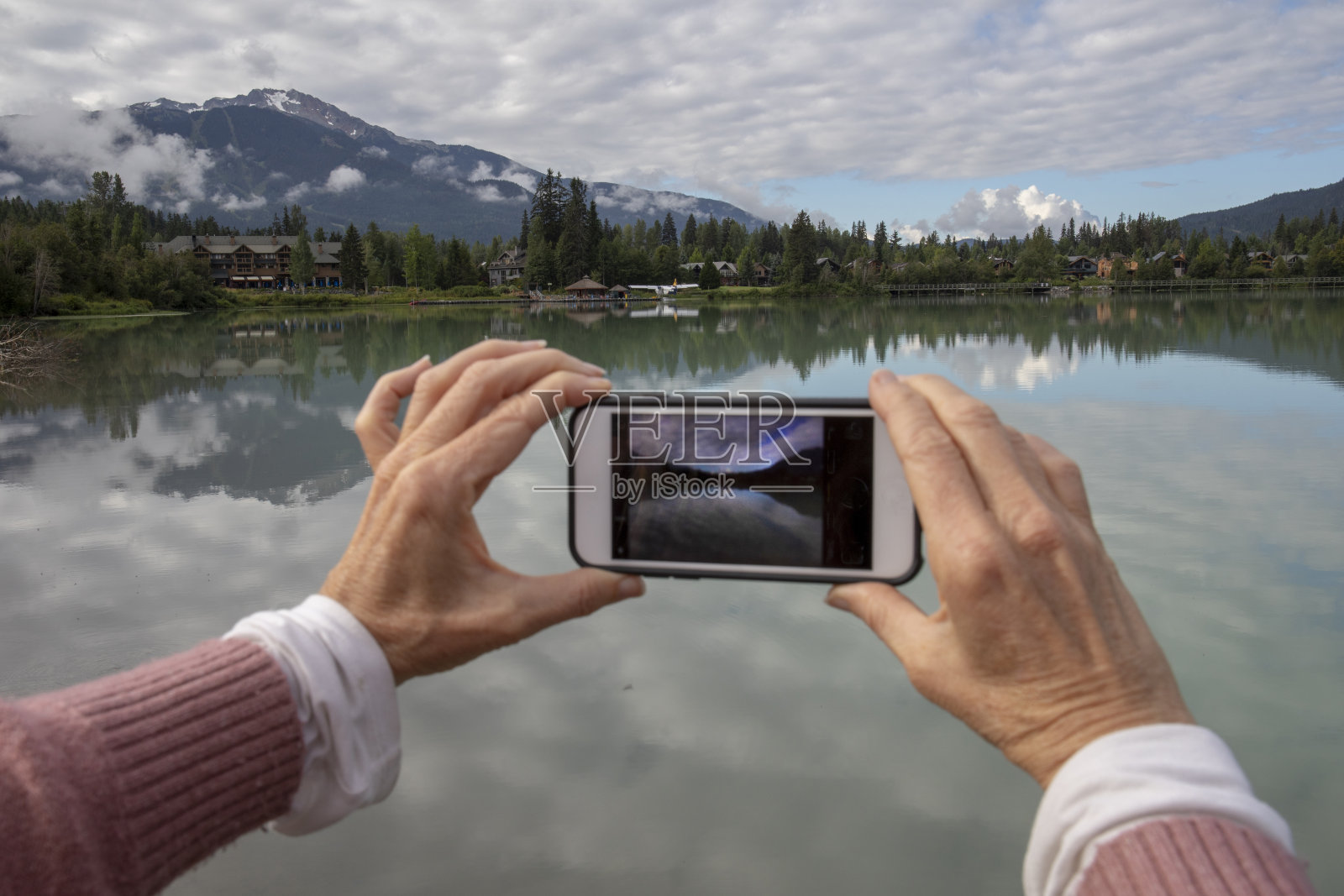 看过去的女人的手臂拍照的倒影在平静的湖照片摄影图片