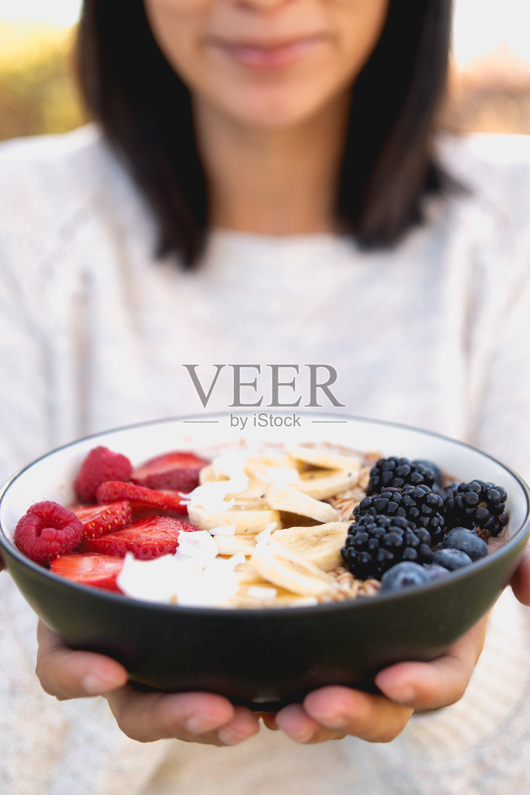 女人拿着一个健康的冰沙碗，里面有水果，格兰诺拉麦片和各种种子照片摄影图片