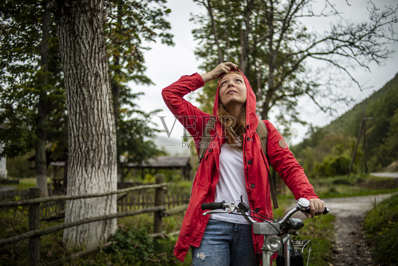 在雨中骑车——一位橙色头发、红色雨衣的年轻女子在雨中骑自行车照片摄影图片