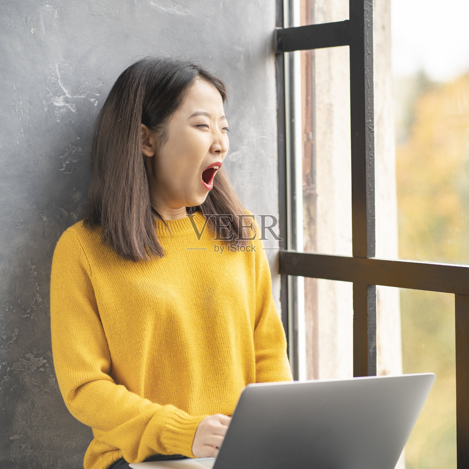亚洲女性因过度劳累而打哈欠。穿亮黄色毛衣的年轻女士照片摄影图片