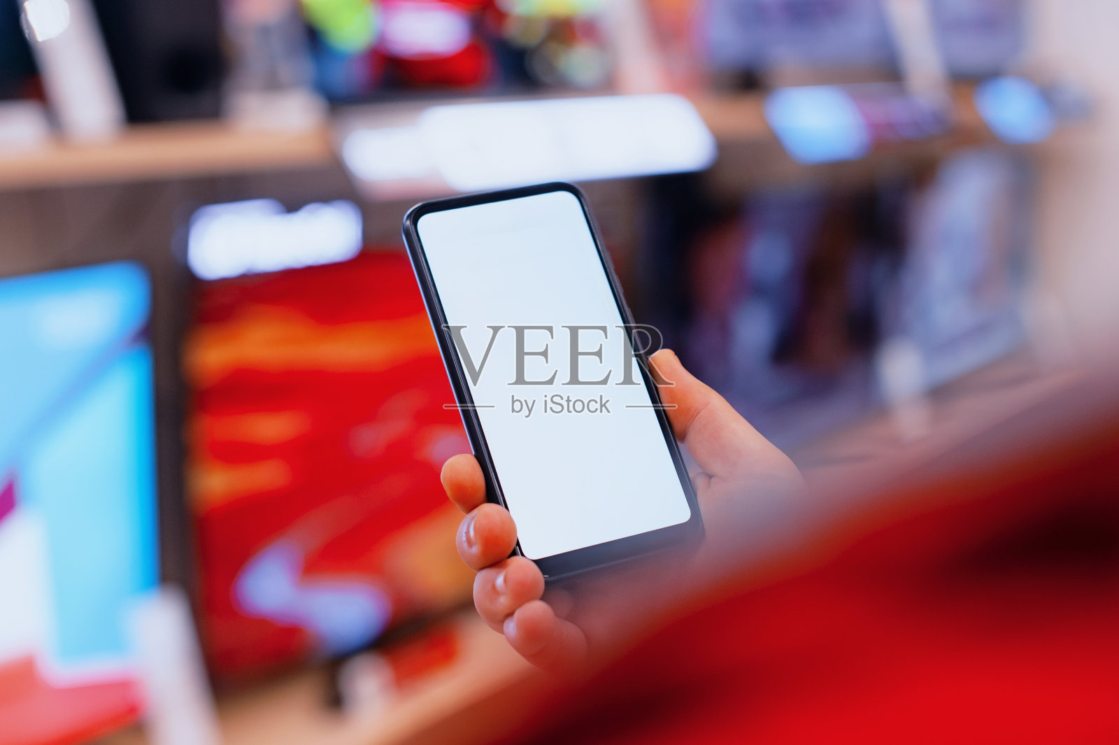 一个男人手里拿着一个白色屏幕的智能手机模型。商店里电视背景上的手机。照片摄影图片