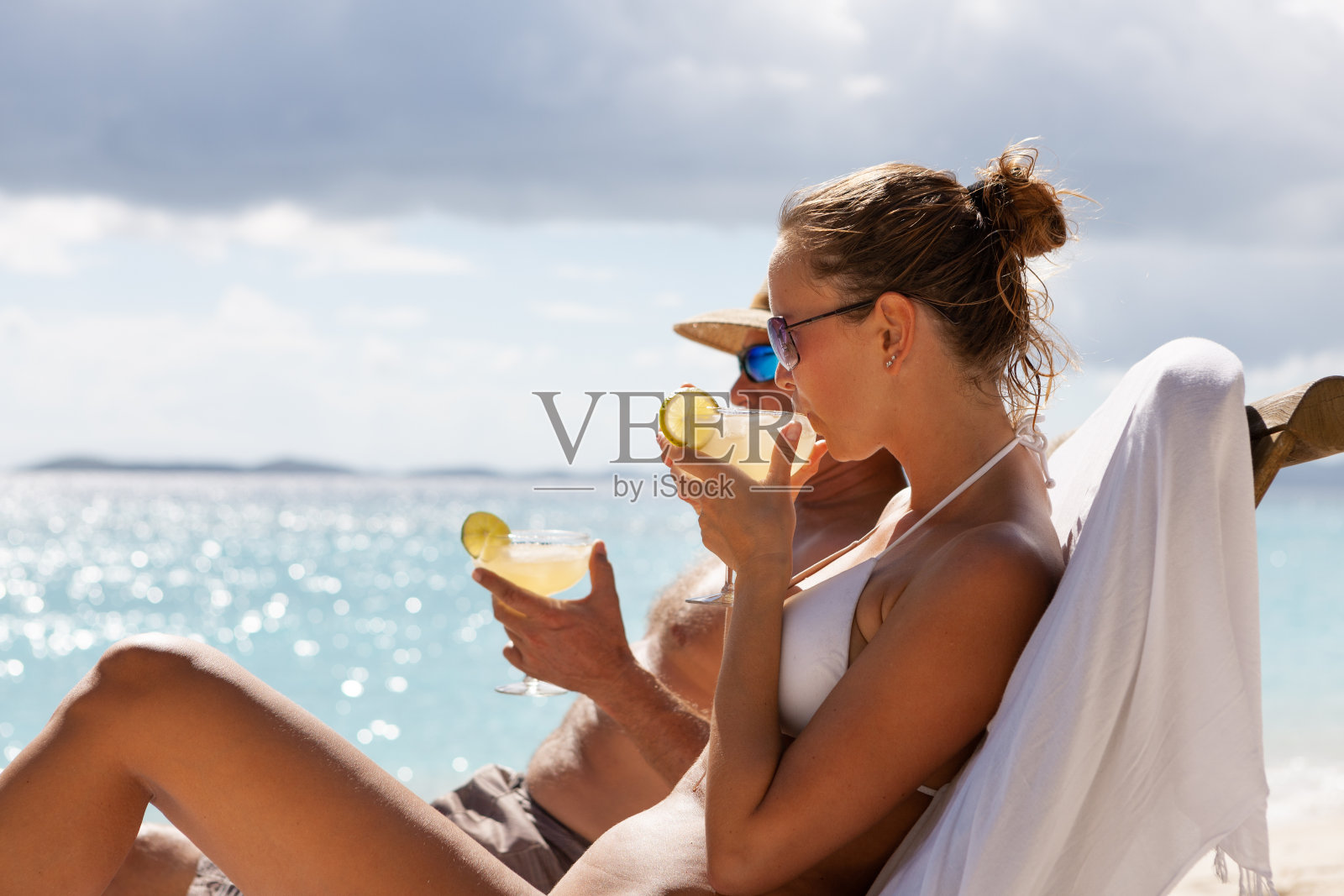 一对夫妇在热带海滩的柚木躺椅上喝着鸡尾酒放松照片摄影图片