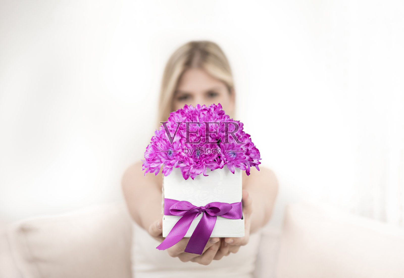 一位年轻的金发女郎手里拿着一束粉红色的菊花，放在一个装饰盒里。照片摄影图片