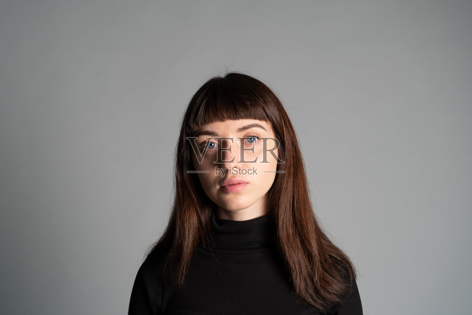 近距离拍摄一个年轻女子的照片，背景是普通的灰色照片摄影图片