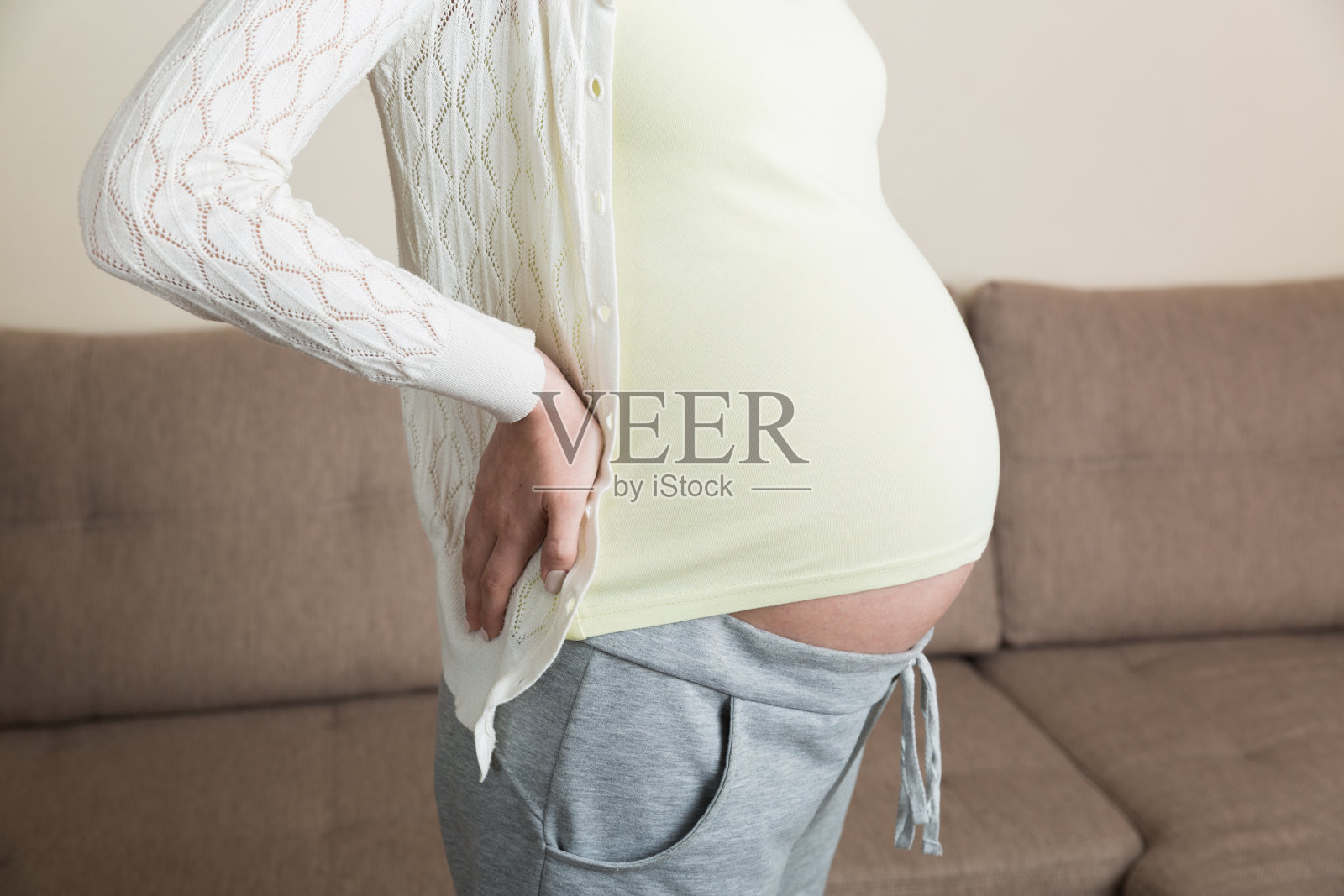 美丽的孕妇触摸她的肚子，并保持一只手在她的背部在家里照片摄影图片