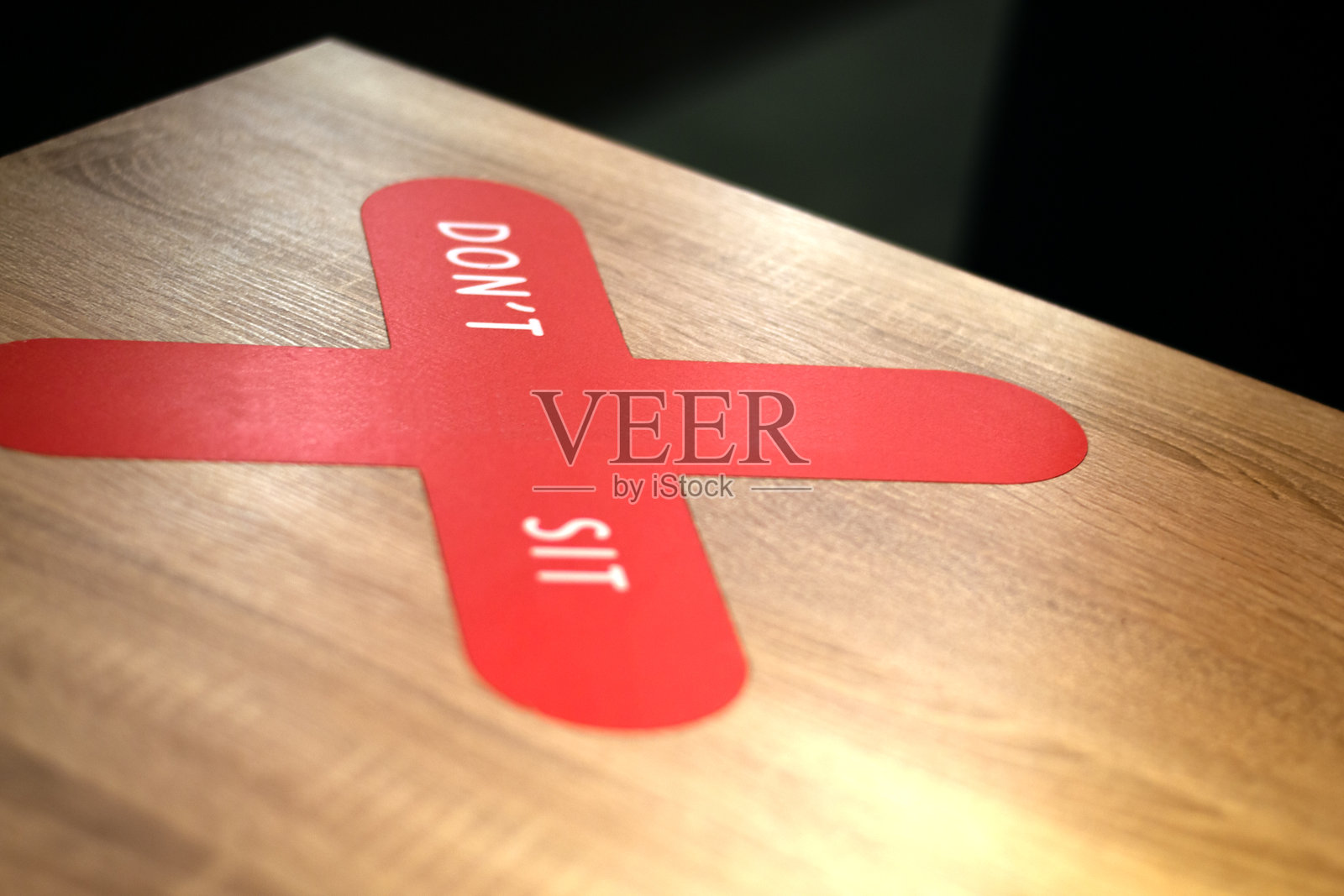 红色警告贴纸的边上有一个十字，上面写着“不要坐”。呼吁在新的隔离现实和条件下保持社会距离。模糊的照片摄影图片