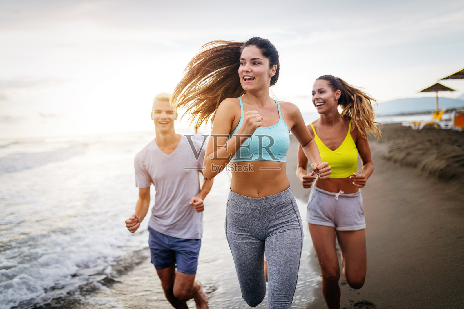 一群年轻的朋友在海滩上跑步和锻炼照片摄影图片