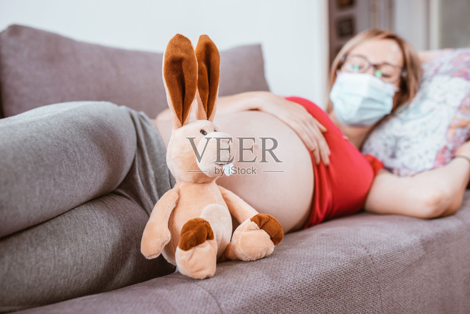 微笑的孕妇躺在沙发上，脸上戴着防护面具照片摄影图片