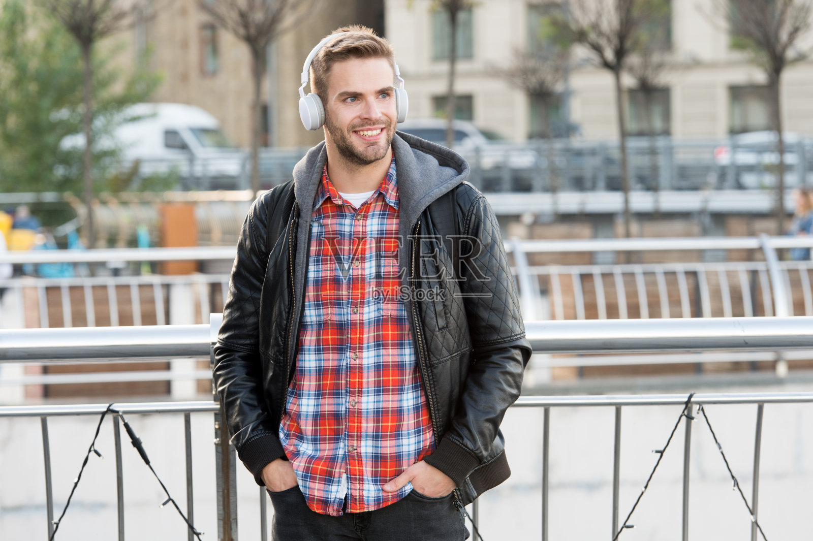 街拍。快乐的家伙戴着耳机在城市户外。帅哥听着立体声耳机里的音乐。现代设计耳机。新技术。耳机在任何地方照片摄影图片