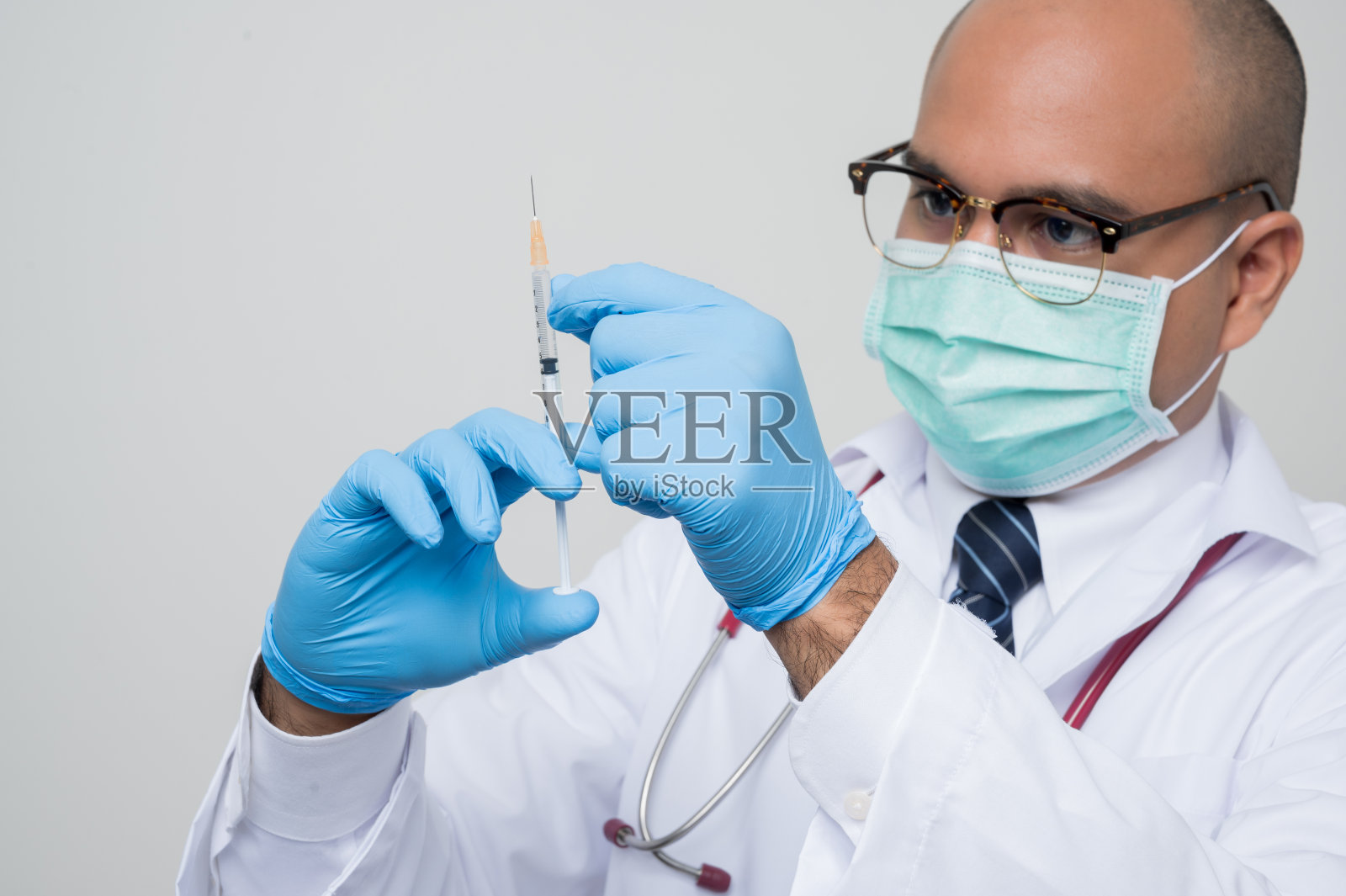 亚洲秃顶医生，白大褂，听诊器，蓝色手套拿着和“触摸一个注射器孤立的白色背景。”照片摄影图片