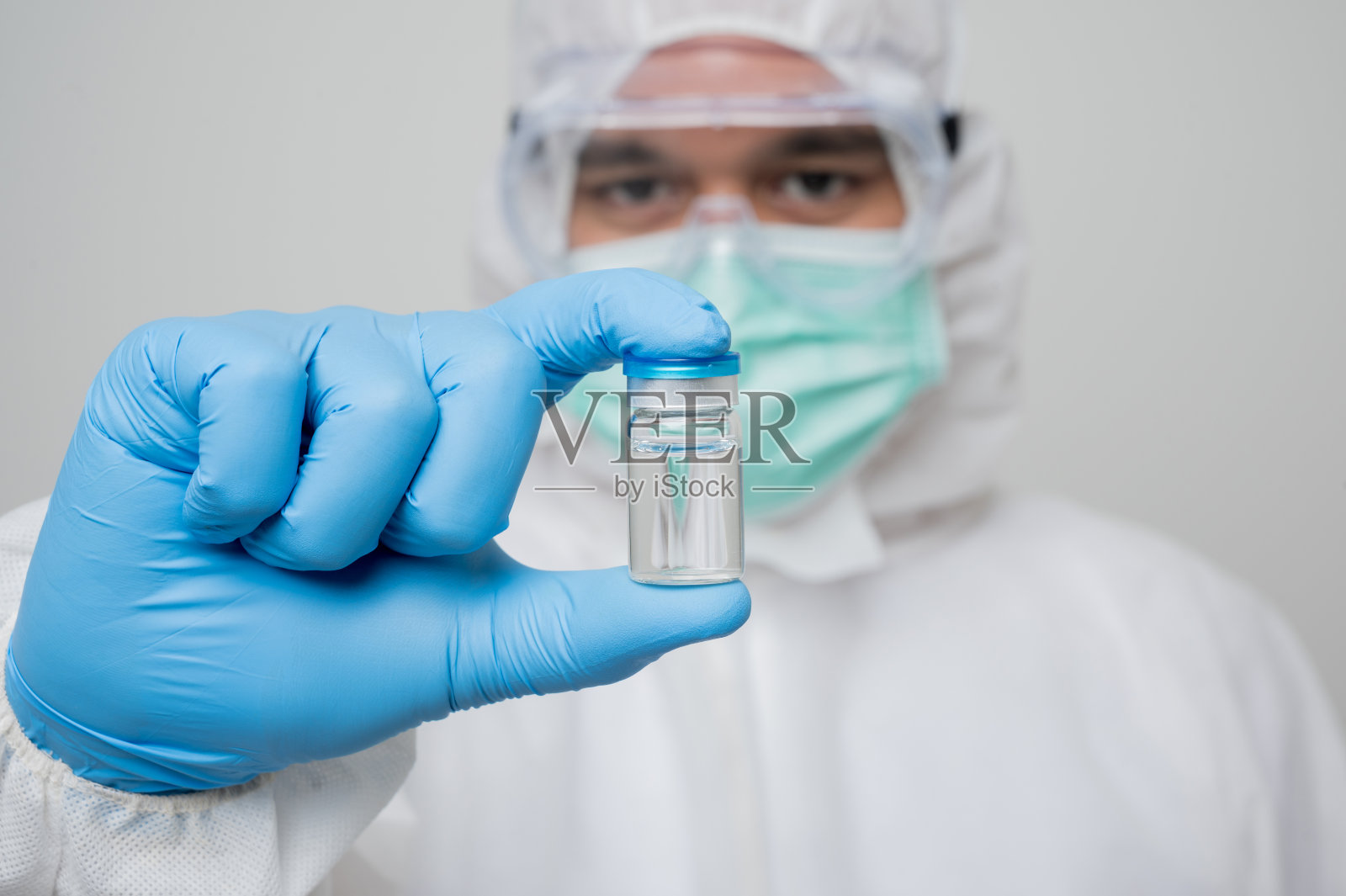 一幅病毒学家的肖像，穿着防护服，手持隔离的疫苗瓶在白色背景上。个人防护装备概念。照片摄影图片