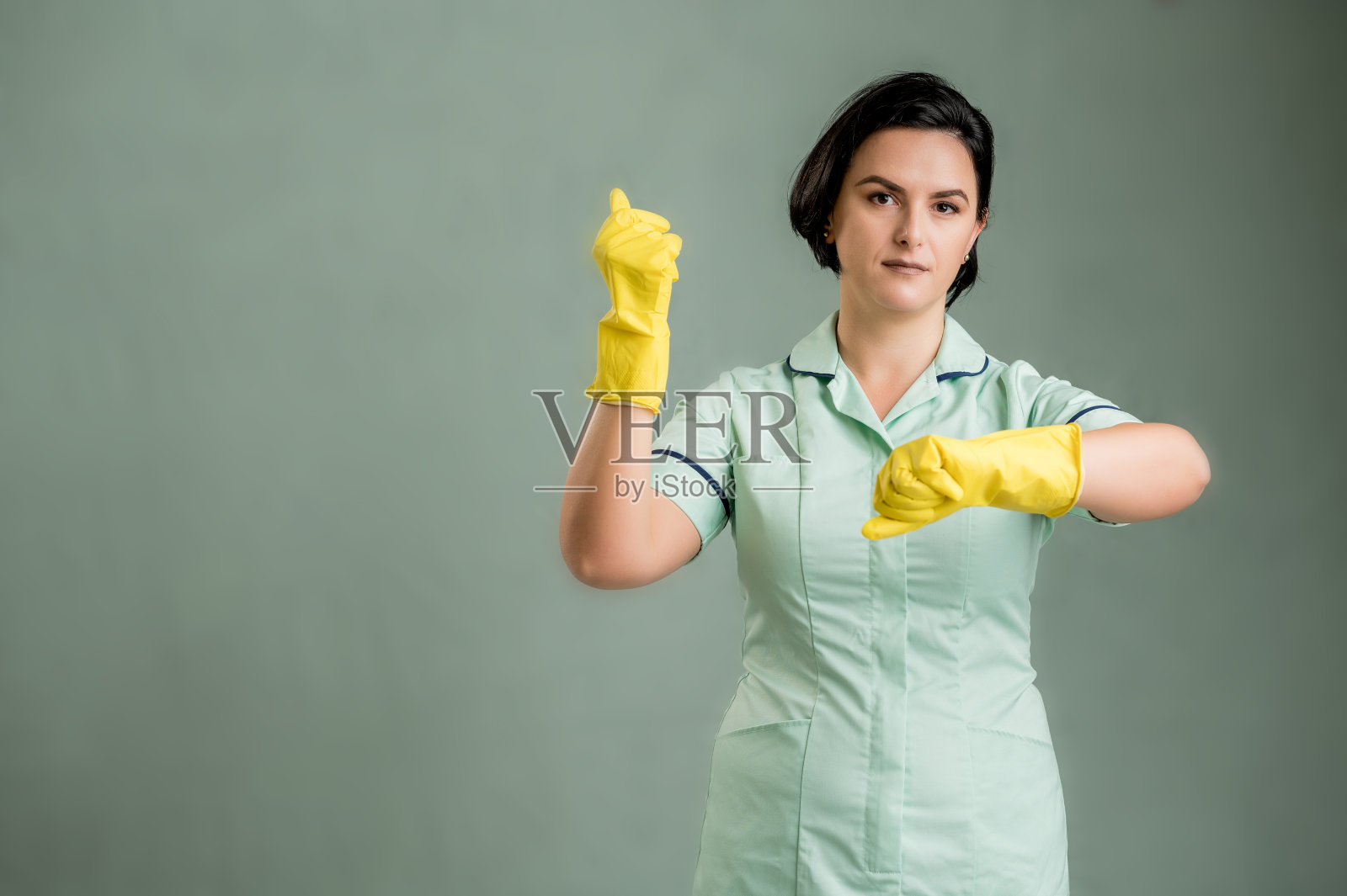 年轻的清洁女工穿着绿色的衬衫和黄色的手套显示时间是金钱的姿态照片摄影图片