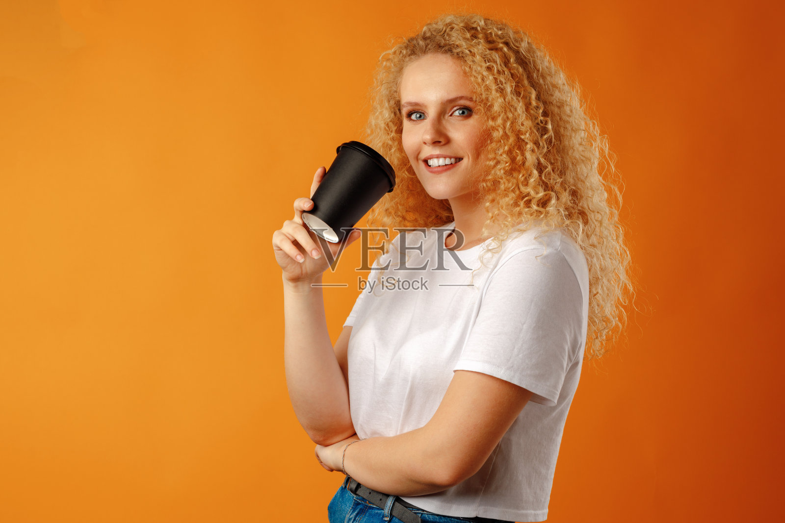 迷人的年轻女子站在和喝热饮料的黄色背景照片摄影图片