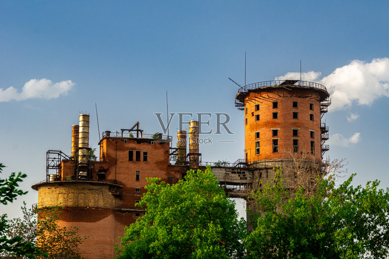 一座废弃的砖砌工业建筑，有避雷针和生锈的烟囱，映衬着布满积云的蓝天照片摄影图片