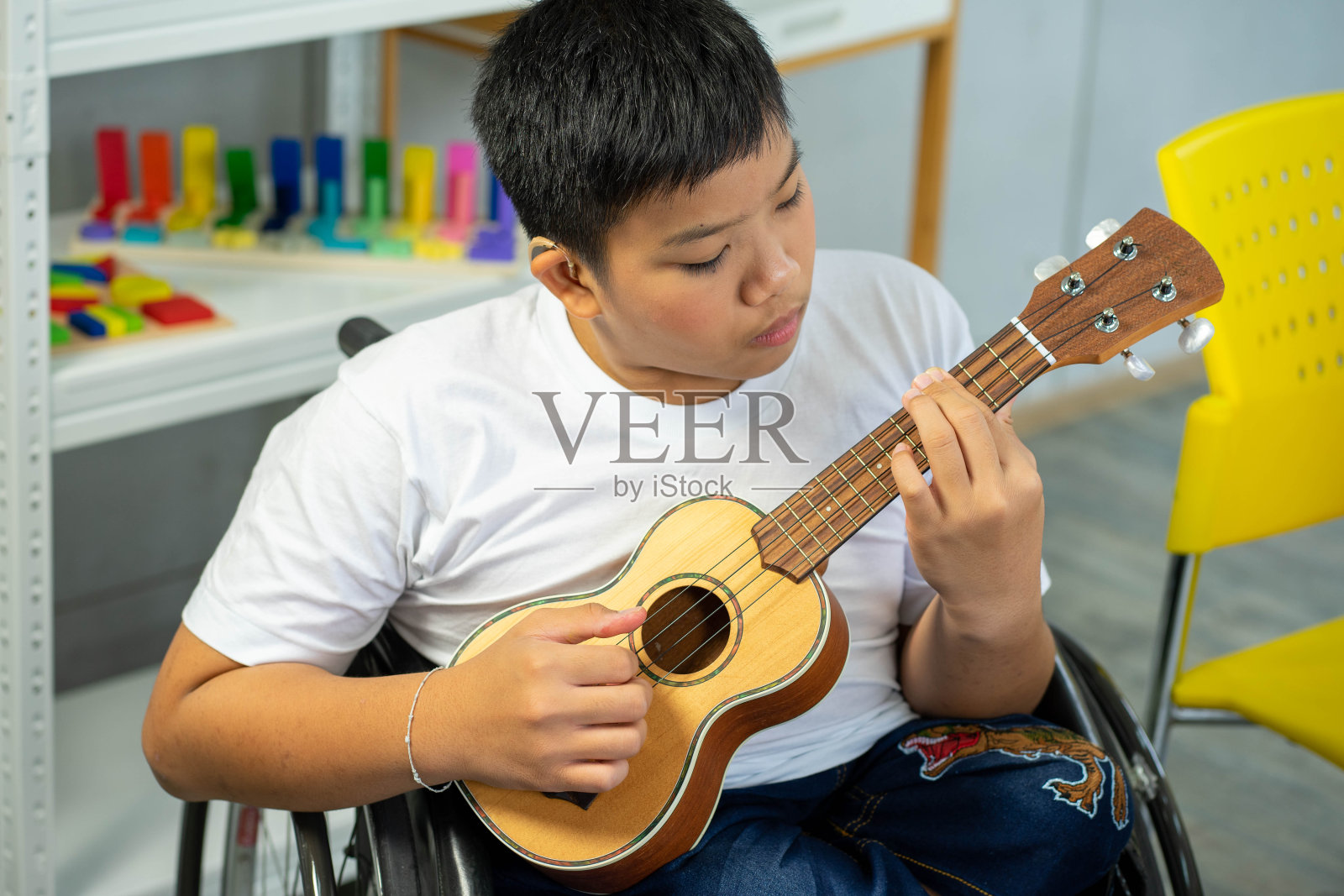 残疾儿童在轮椅上用吉他演奏音乐，自闭症儿童在特殊教室演奏照片摄影图片