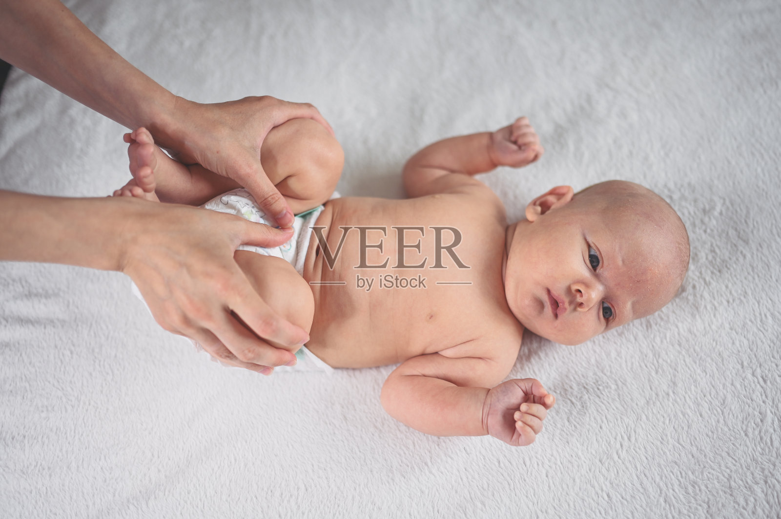 妈妈正在给躺在婴儿床上的可爱的、情绪化的、有趣的新生小男孩换尿布照片摄影图片