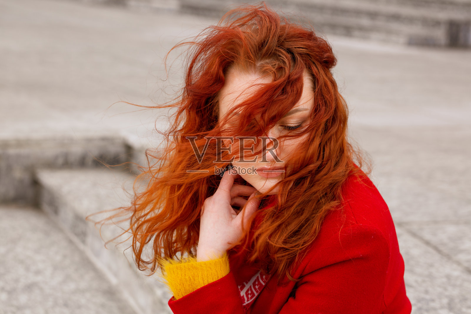 街上穿着红色外套的年轻女人的特写肖像，头发垂在脸上，孤独和悲伤的概念照片摄影图片