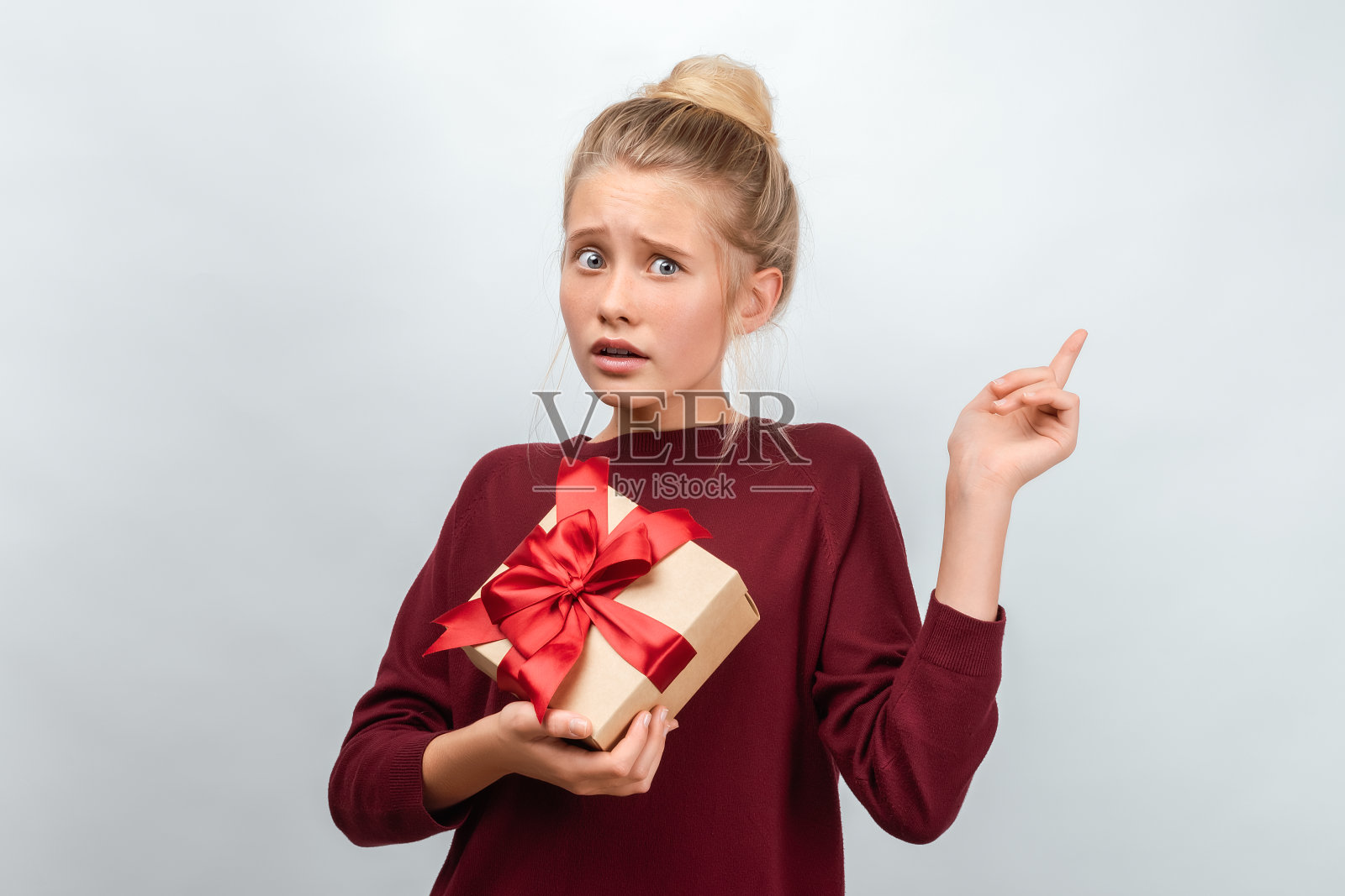 画像困惑的金发女孩12-15岁拿着用丝带装饰的礼物。工作室拍摄白色背景照片摄影图片