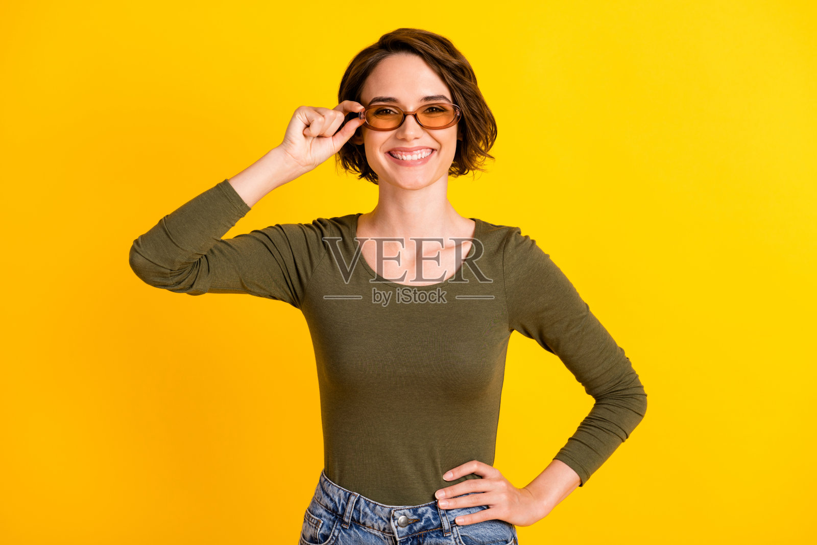 女孩的照片，手戴眼镜，手臂，臀部微笑，戴太阳镜，绿色衬衫孤立亮黄色背景照片摄影图片