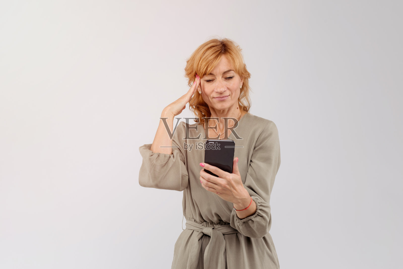 一个兴奋的成年女性的肖像，在白色的背景下看着手机。空的空间照片摄影图片