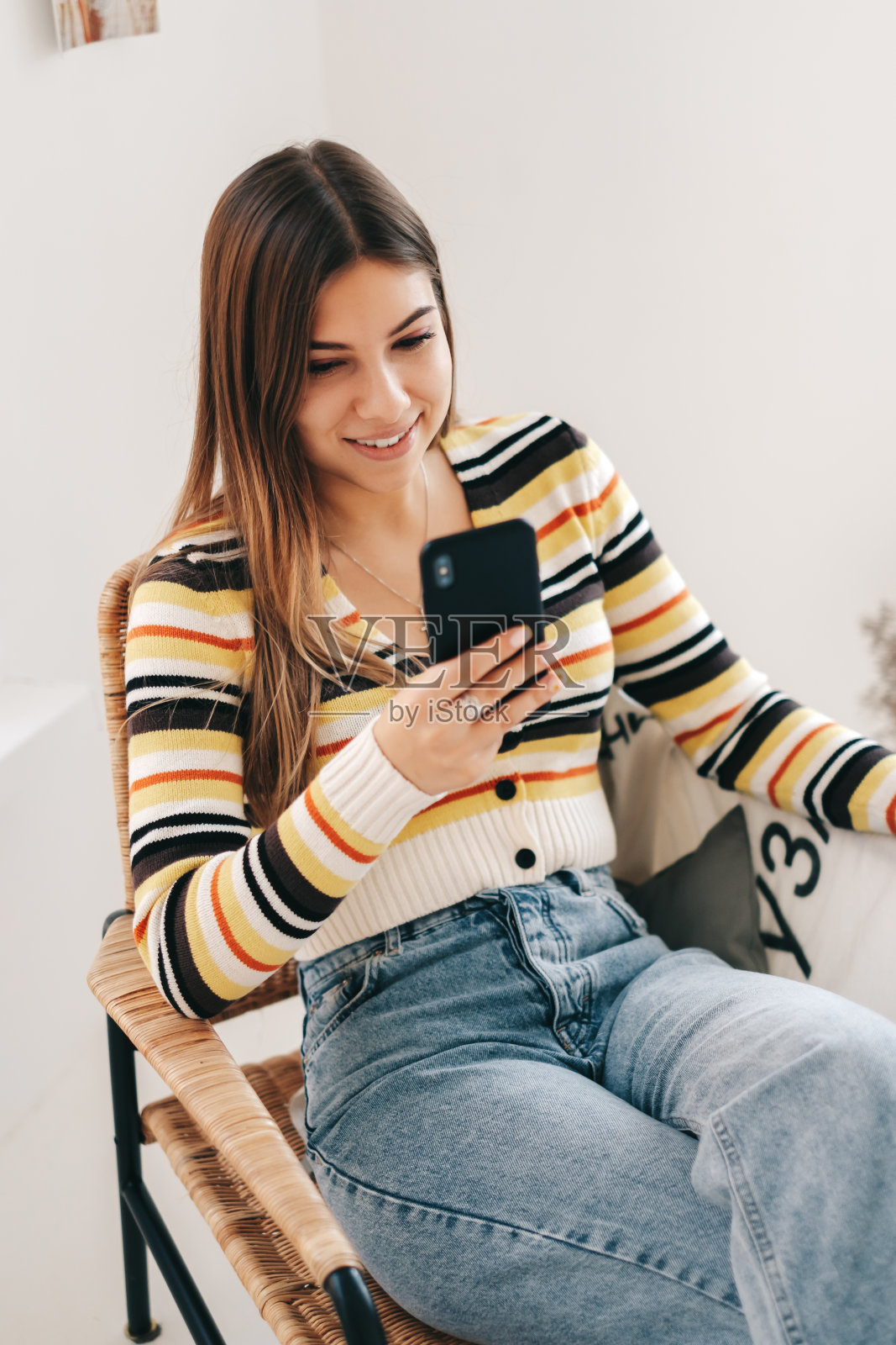 微笑的白人妇女使用智能手机，坐在家里的扶手椅上。照片摄影图片