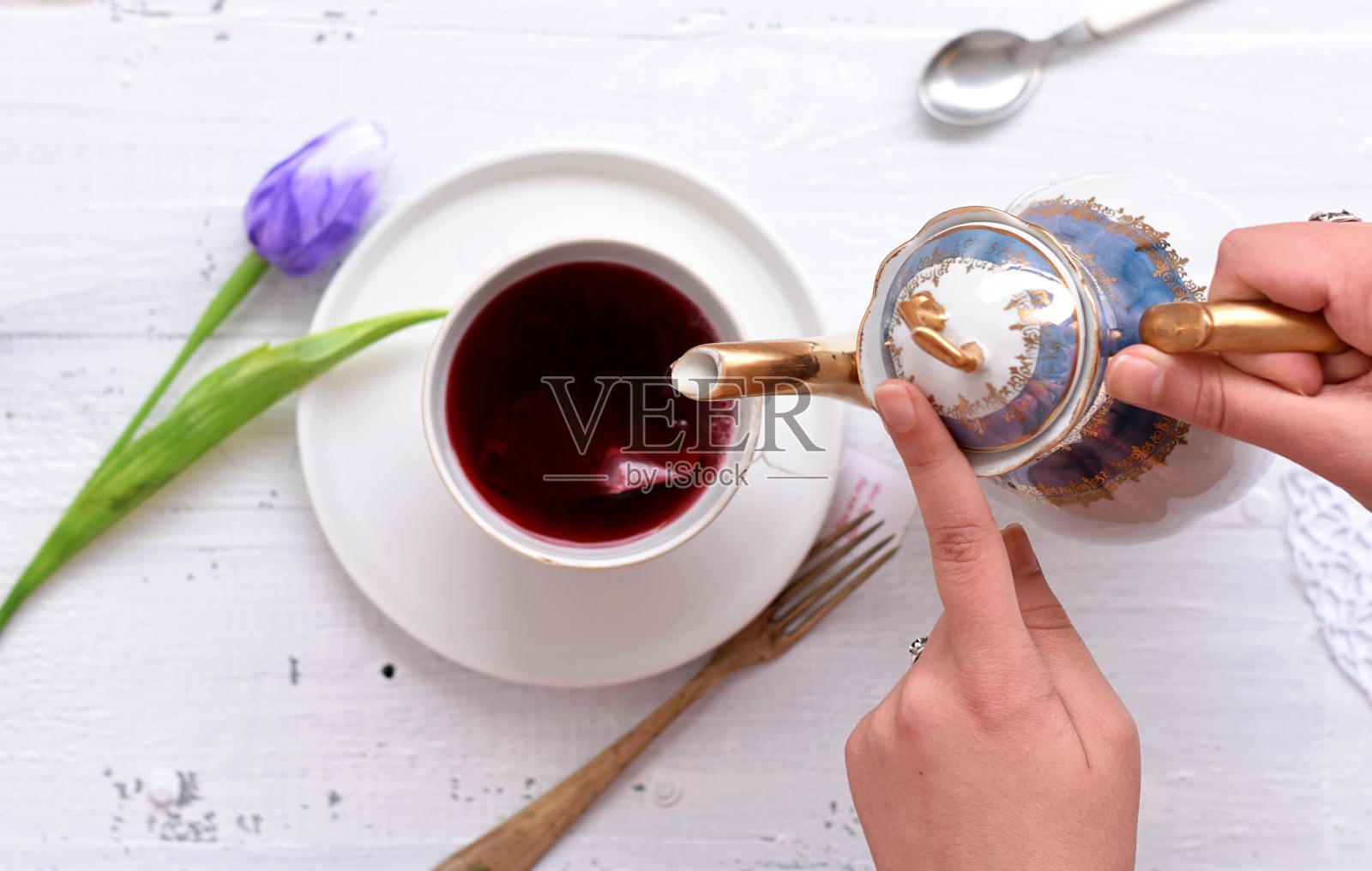 一个女人把热腾腾的红茶倒进白色木桌上的杯子里/特写静物美食摄影照片摄影图片