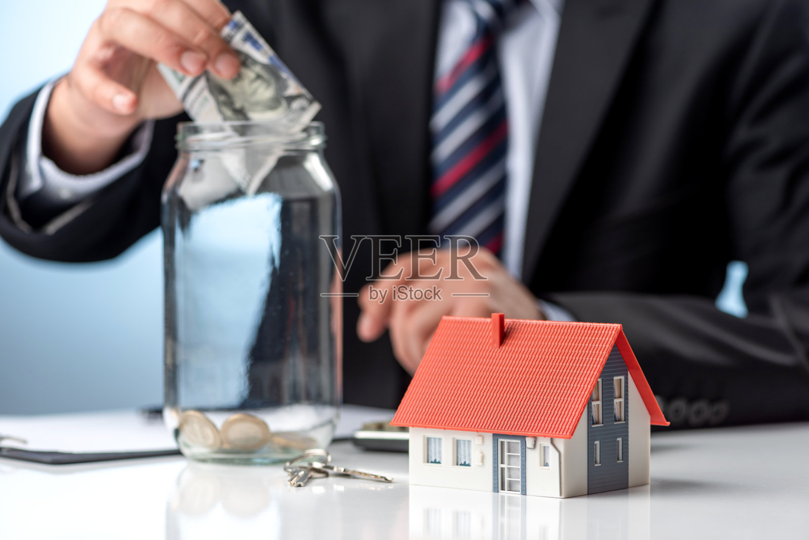 商人在瓶子里扔了几百美元，旁边还有模型房照片摄影图片