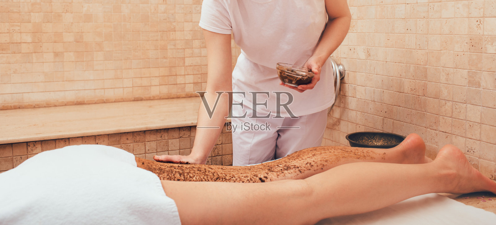 按摩师把泥擦在女人的腿上。给女人去皮会让她的腿光滑。特写镜头照片摄影图片